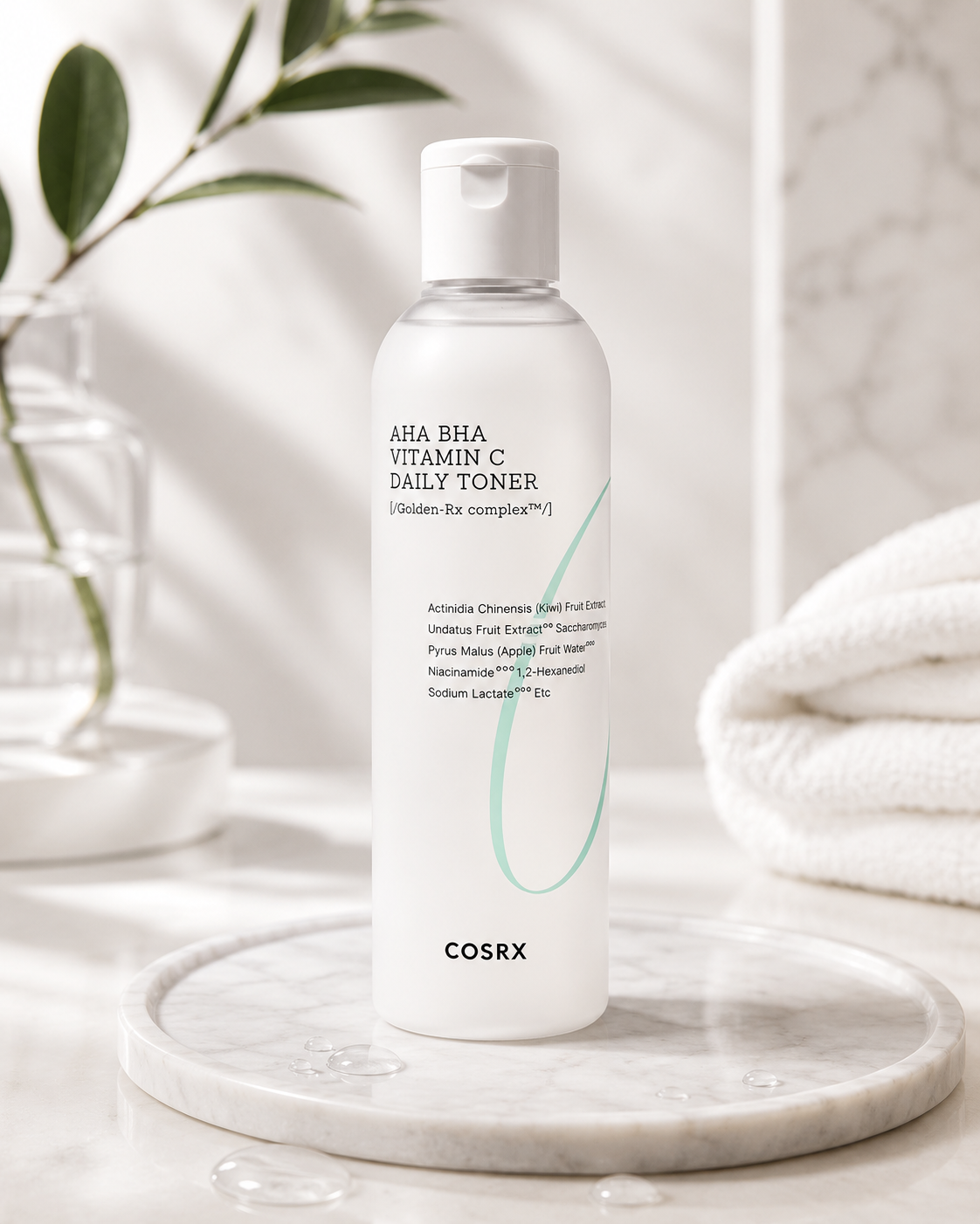 COSRX Refresh AHA BHA Vitamin C Daily Toner displayed on a marble tray with green botanical leaves, a glass vase, soft towels, and water droplets in a bright spa-inspired setting. Infused with AHA, BHA, Vitamin C, niacinamide, and Golden-RX Complex, this lightweight exfoliating toner helps remove impurities, promote a brighter complexion, smooth rough texture, balance the skin, and deliver refreshing hydration for healthy, glowing skin suitable for everyday use.